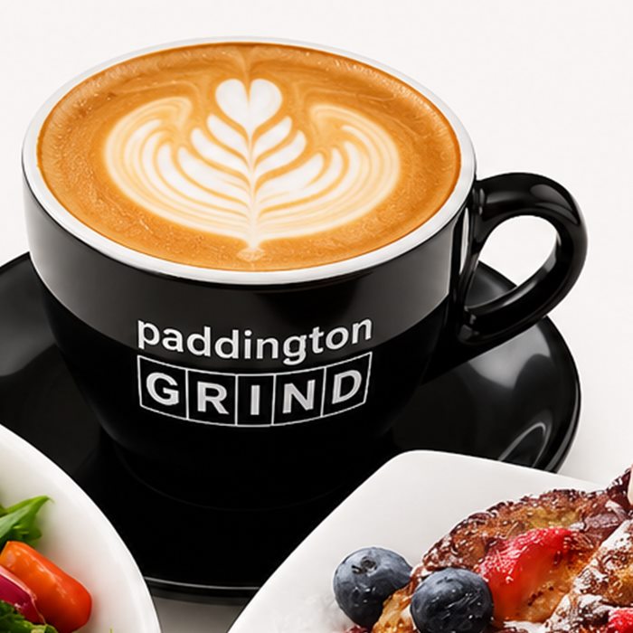A latte with rosetta art in a black Paddington Grind cup and saucer.