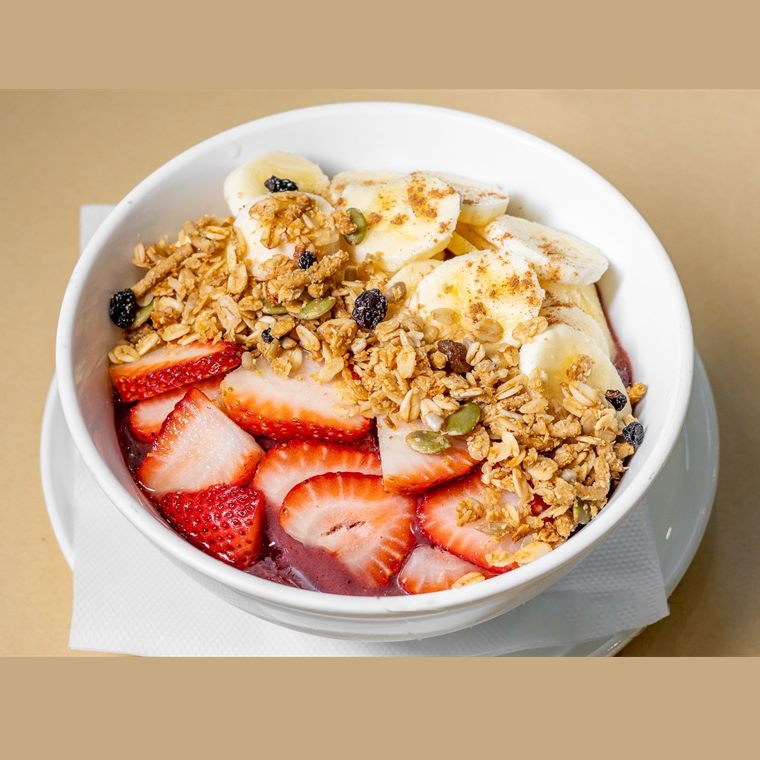 An acai bowl topped with sliced strawberry, banana and toasted muesli.
