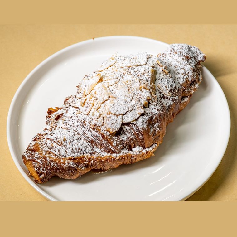 An almond croissant dusted with icing sugar and scattered with flaked almonds.