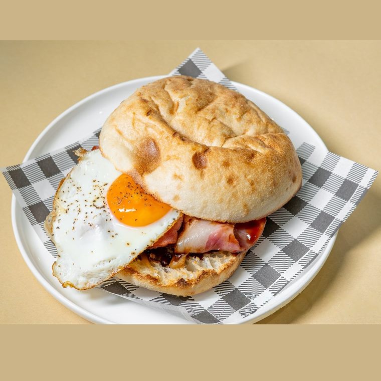 A bacon and egg roll on a crusty white bun, the yolk still running, on a checked paper napkin.