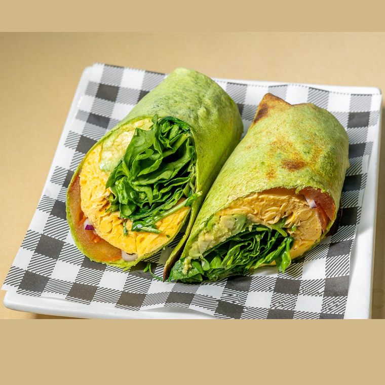 A spinach wrap cut in half, filled with scrambled egg, avocado, tomato and spinach.