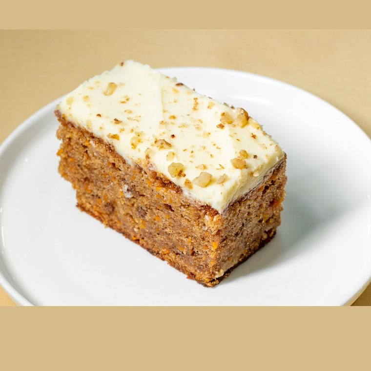 A slice of carrot cake with thick cream cheese icing and walnuts.