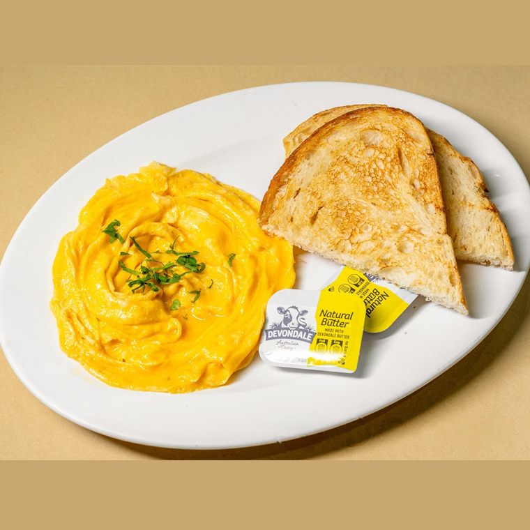 Soft scrambled eggs with two slices of buttered sourdough toast on a white plate.