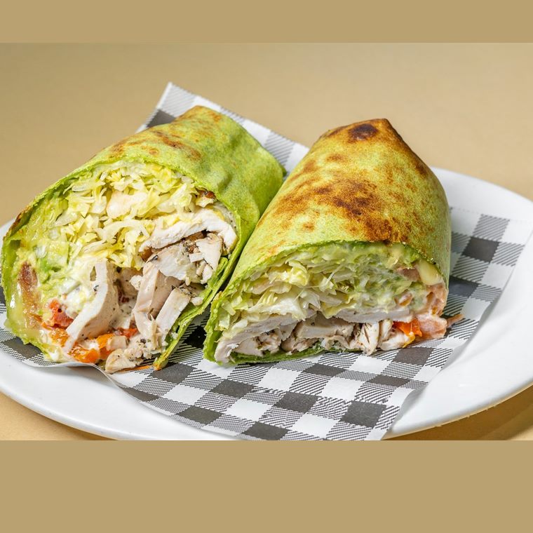A spinach wrap cut in half, filled with grilled chicken, avocado, cheese and salad.