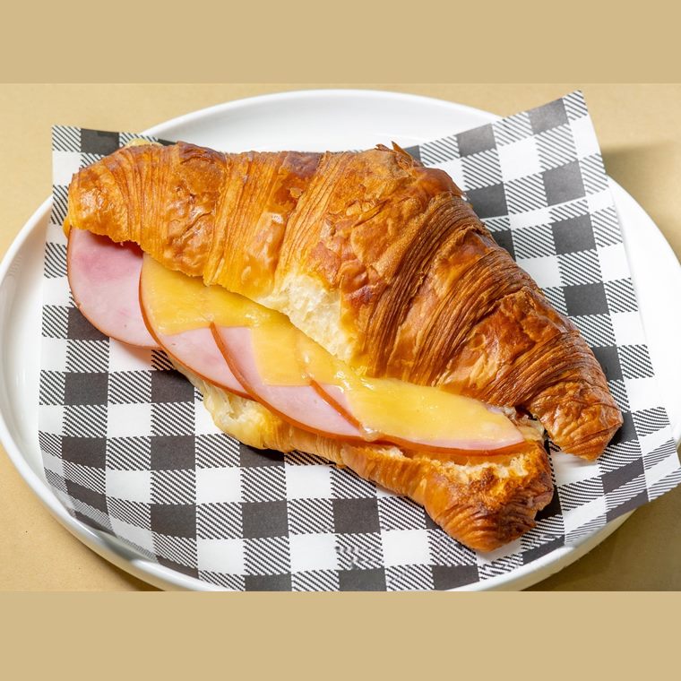 A butter croissant split and filled with shaved ham and melted cheese.