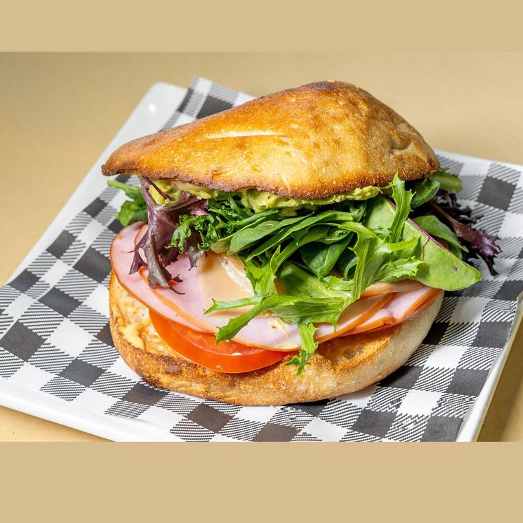 A ham sandwich with cheese, tomato, avocado and mixed lettuce.