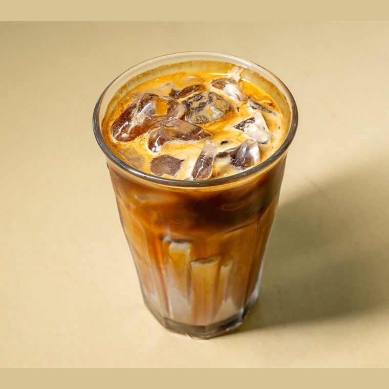 An iced latte in a tall glass, the espresso still marbling through the milk.