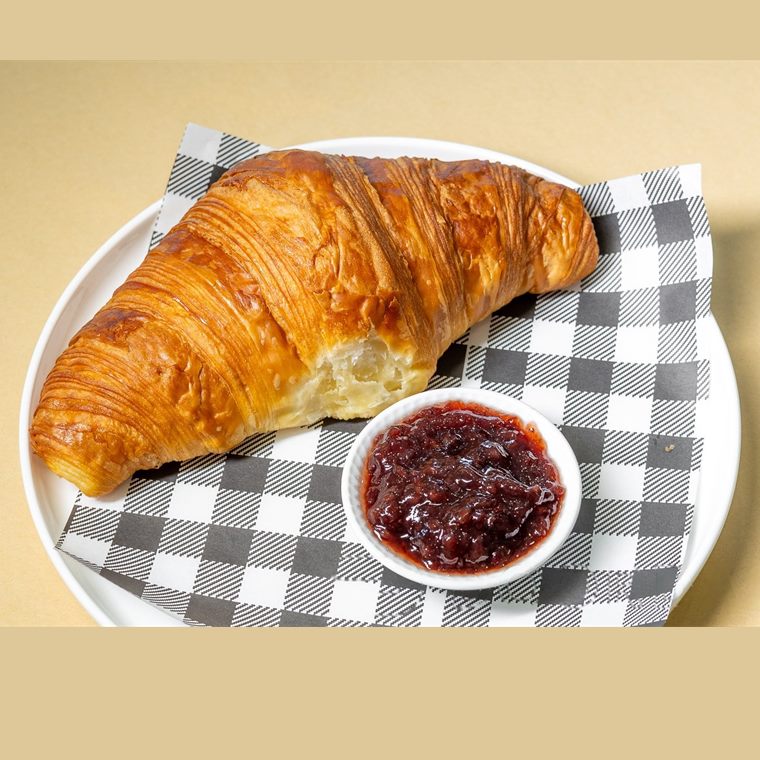 A golden butter croissant served with a small pot of berry jam.