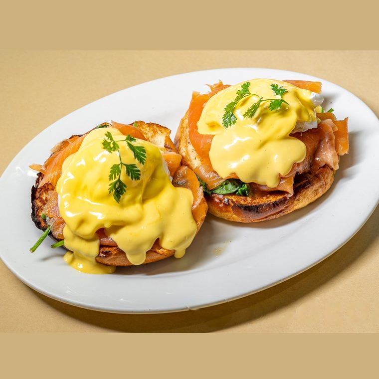 Two toasted muffin halves topped with smoked salmon, poached egg, hollandaise and chives.
