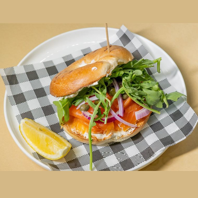 A bagel with smoked salmon, cream cheese, Spanish onion, rocket and capers, with a lemon wedge.