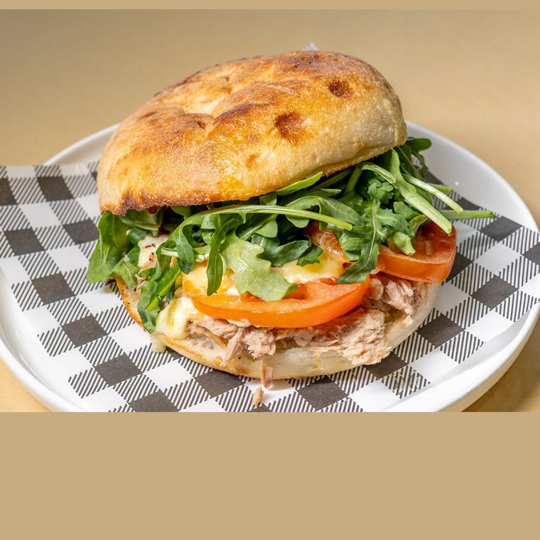 A tuna sandwich on a crusty roll with tomato, cheese and rocket.